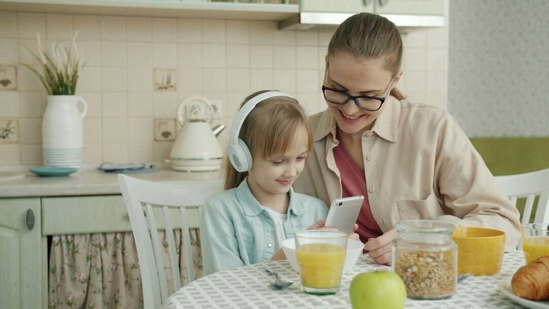 Mother and young daughter using a smartphone together at the kitchen table